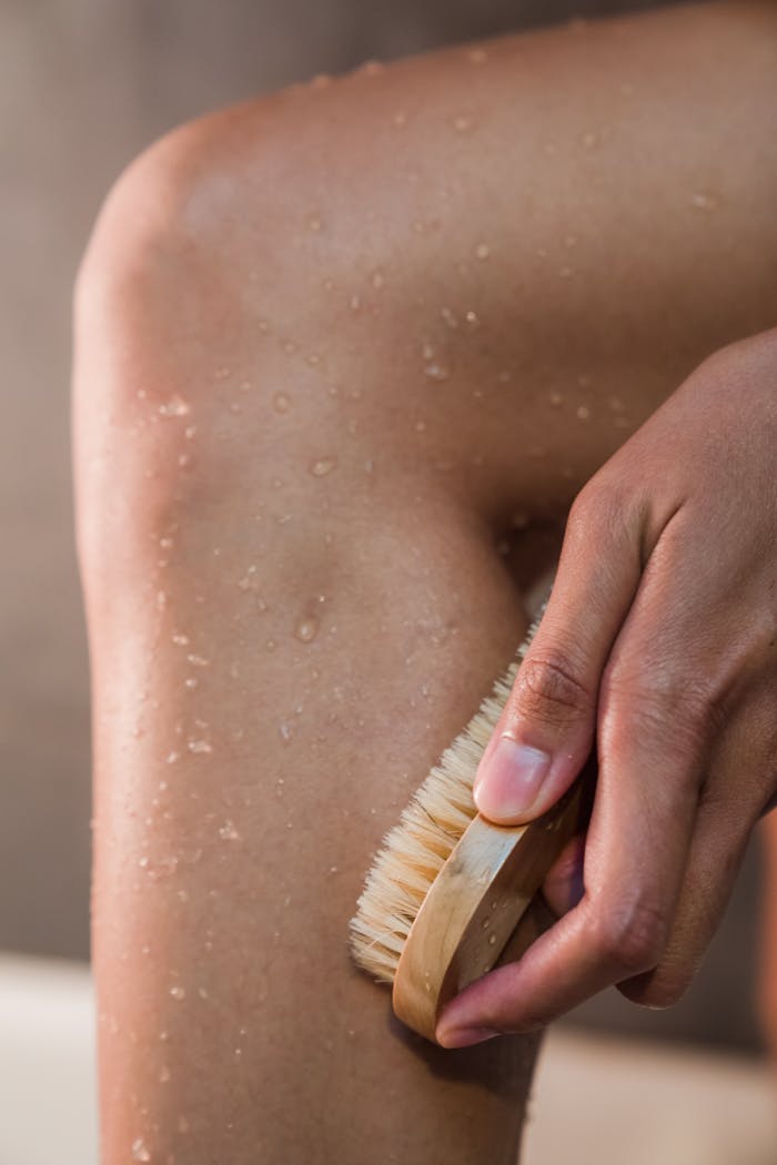 about-us Close-up of a hand using a body brush on a wet leg for personal hygiene and exfoliation.
